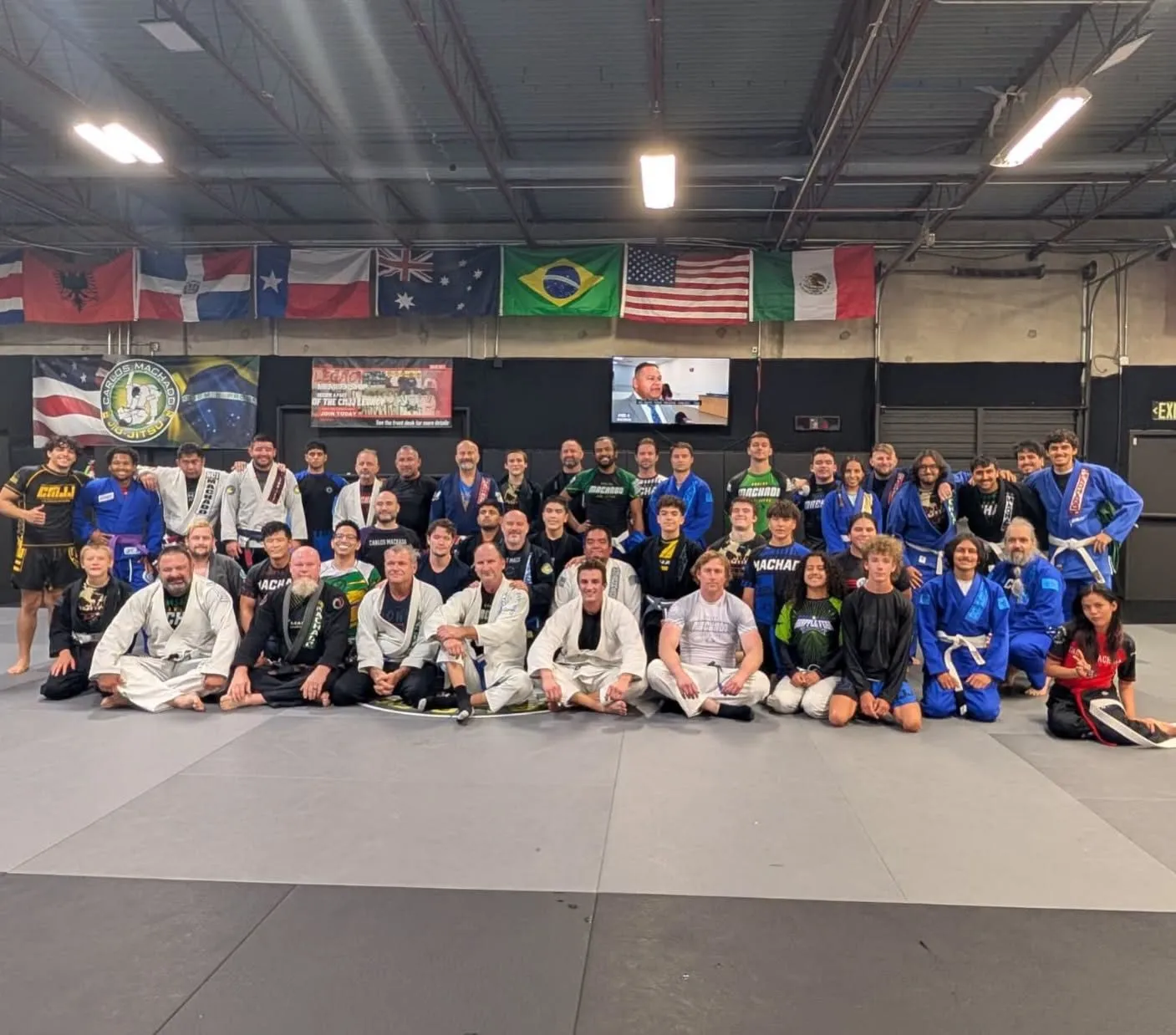 A large group of Machado Method students gathered together on the mat under the Carlos Machado Jiu-Jitsu banner in Carrollton, TX