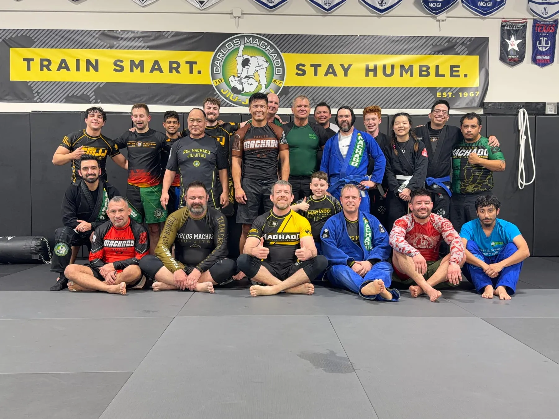 The adult Brazilian Jiu-Jitsu class at Machado Method Carrollton gathered together under the Train Smart, Stay Humble banner