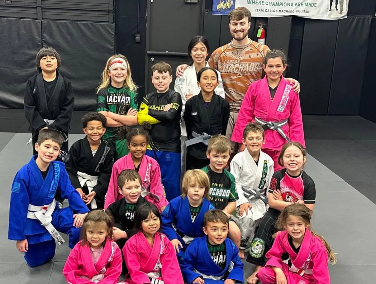 Machado Method kids lined up in their gis under the Team Carlos Machado banner in Carrollton, TX