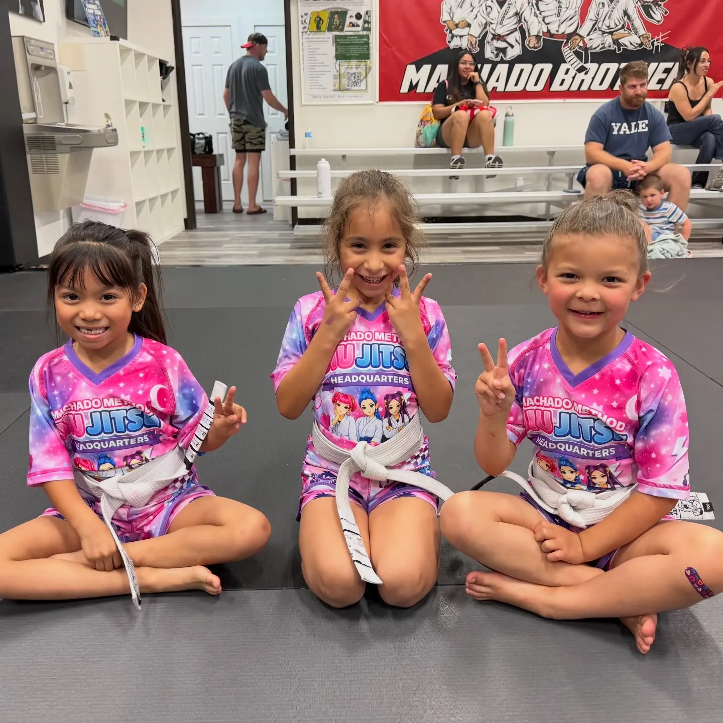 Three young Cubs students in pink Machado Method gis smiling on the mat in Carrollton, TX