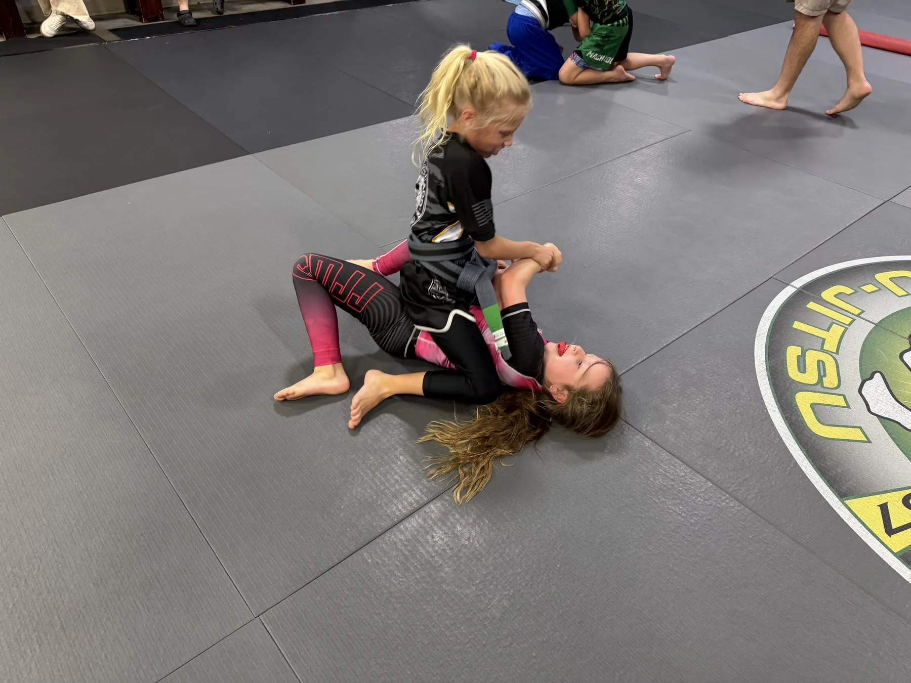 Three young Cubs students in pink Machado Method gis smiling on the mat in Carrollton, TX